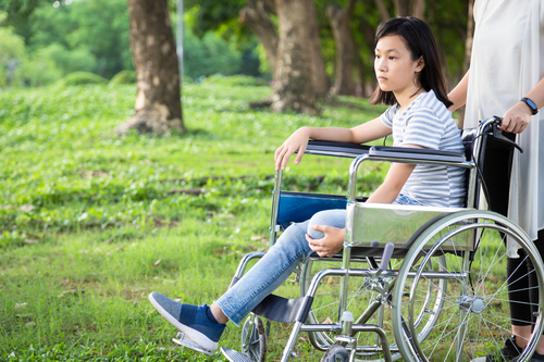 Disabled daughter in wheelchair feeling sad,asian little child girl with depressive symptoms,left leg amputee,crippled,depression,female caregiver or mother care,support in outdoor park,disability concept