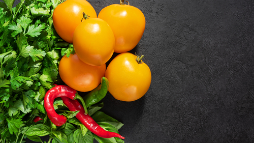 Fresh seasonal vegetables: yellow tomatoes, parsley, basil and red chili pepper on black background. Top view. Copy space
