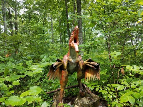 an oranged feathered dinosaur spreading its wings in the woods or forest