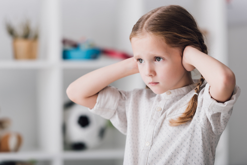 close-up portrait of little child covering ears with hands and looking away