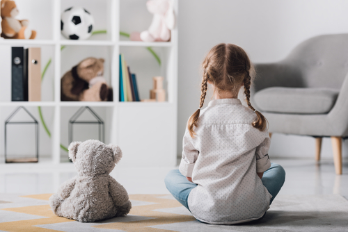 rear view of little child in white shirt sitting on floor with teddy bear