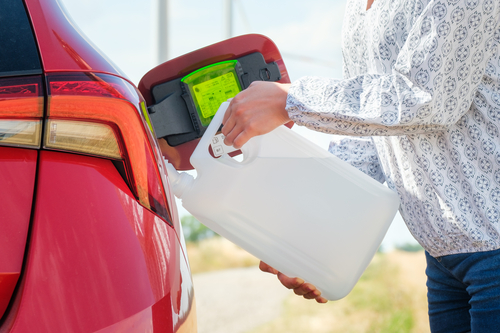 Close up woman refilling the red car with fuel or a diesel engine fluid from canister in the field. 