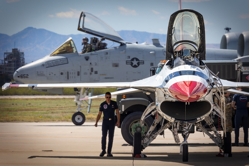 The US Air Force Thunderbirds ground crew work on aircraft while an A-10 Thunderbolt II passes in the background at the 2023 Thunder and Lightning Over Arizona at Tucson, Arizona.
