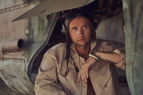 Close-up portrait of a mechanic in uniform and flying near, standing under an old bomber airplane in the open air museum.