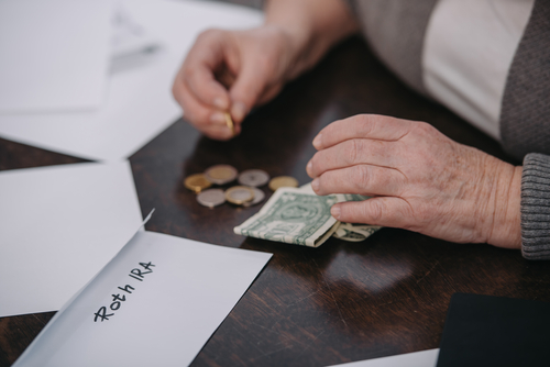 cropped view of couple woman counting money near envelope with 'roth ira' lettering 