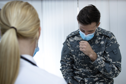 Soldier in uniform with face mask coughing at doctor's office. Military man complaining on corona virus symptoms.