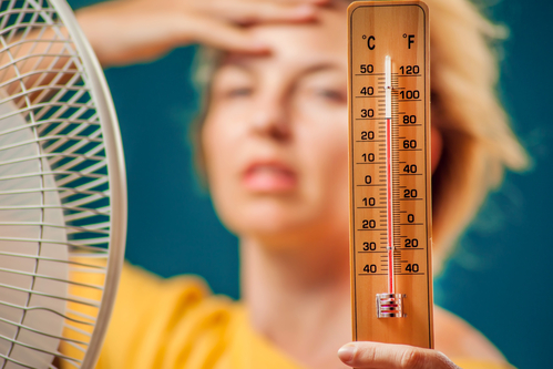 A portrait of woman in front of fan suffering from heat holding thermometer. Hot weather concept