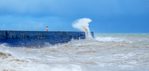 A harbour wall with a rough sea crashing against it and a lighth
